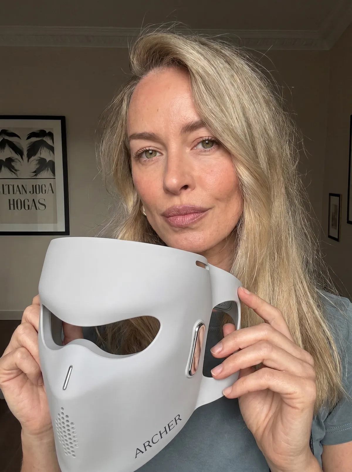 Woman holding the ARCHER LED face mask at home, showing its facial contour.