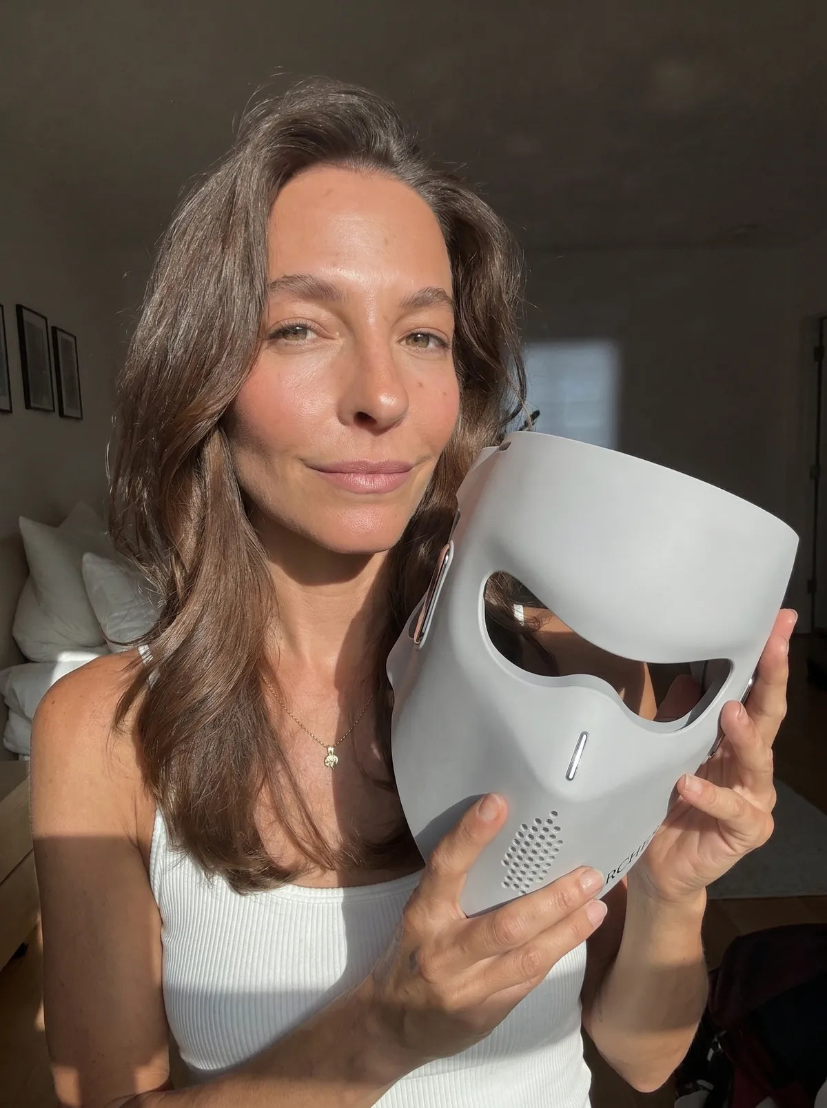Woman with glowing skin holding the ARCHER LED face mask in natural light.